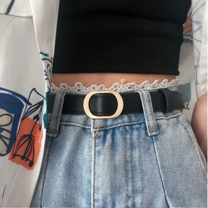 Nahaufnahme eines schwarzen Ledergürtels mit goldener ovaler Schnalle auf blauer Jeans
