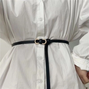 Ceinture fine en cuir noir minimaliste avec boucle dorée sur une chemise blanche
