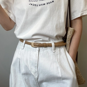 Detail of a slim khaki leather belt with a matte gold buckle on white trousers