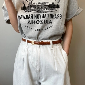 Close-up of vintage brown leather belt with gold buckle on white trousers and grey t-shirt