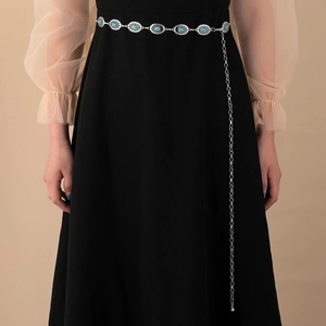 Détail de la ceinture chaîne en métal argenté avec pierres turquoise sur robe noire