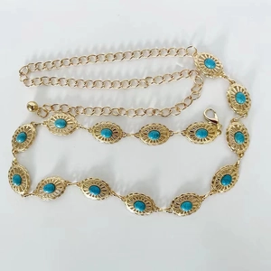 Détail d'une chaîne de taille bohème en métal doré avec pierres turquoise et motifs concho