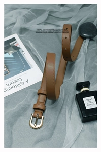 Détail d'une ceinture fine en similicuir marron avec boucle fer à cheval dorée sur magazine