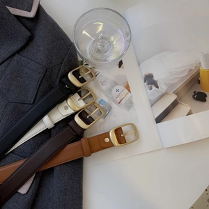 Detailaufnahme von vier schmalen Ledergürteln in Schwarz Weiß und Braun mit Goldschnallen