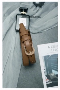 Détail d'une ceinture fine en simili cuir marron avec boucle en U dorée sur fond texturé