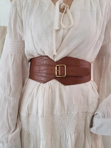 Close-up of a wide brown crocodile pattern waist belt with a golden square buckle on a dress