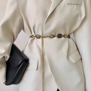Vintage gold metal chain belt with engraved oval links on a beige blazer jacket