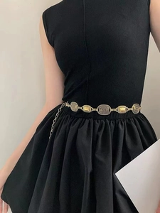 Close-up of vintage golden waist chain with engraved oval textures on black dress