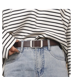 Close-up of a minimalist brown leather belt with silver buckle worn on blue jeans