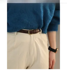 Detail eines dunkelbraunen schmalen Ledergürtels mit Messingschnalle auf cremefarbener Hose