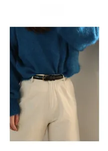 Detail eines schmalen schwarzen Ledergürtels mit goldener Metallschnalle auf weißer Hose