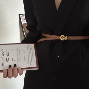 Detail of a thin camel leather belt with a golden knot buckle on a black suit blazer