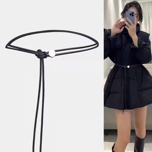 Détail d'une fine ceinture en corde noire avec boucle argentée sur un manteau noir