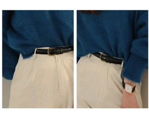 Detail eines schmalen schwarzen Ledergürtels mit Bronzeschnalle auf einer weißen Hose