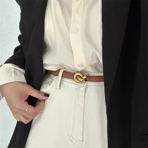 Detail showing a vintage brown leather belt with a stylish golden twisted knot buckle