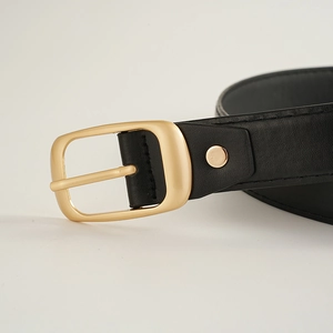 Détail macro d'une ceinture en cuir noir mat avec boucle ardillon en métal doré poli