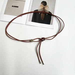 Gros plan d'une ceinture tressée marron-rouge avec des sequins métalliques sur fond blanc
