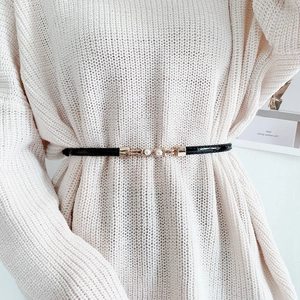 Détail d'une ceinture noire fine avec boucle dorée perlée sur un pull en maille
