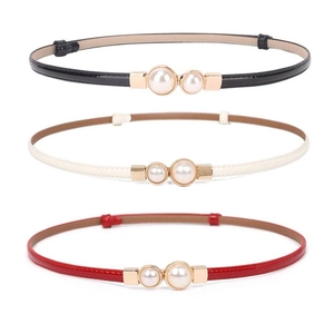 Detail of skinny patent leather belts with gold buckles and pearls in black, white, and red