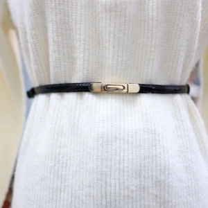 Detail of slim black patent leather belt with golden metal buckle on white dress