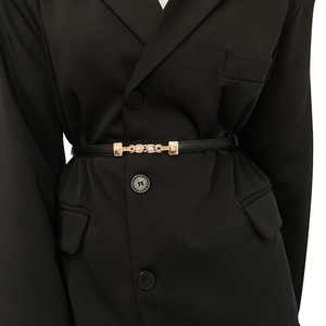 Détail d'une fine ceinture en cuir noir avec boucle dorée perlée sur une veste