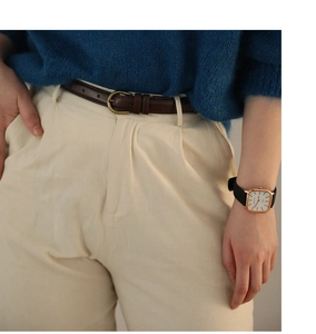 Detail eines schmalen braunen Ledergürtels mit goldener Schnalle auf beiger Hose