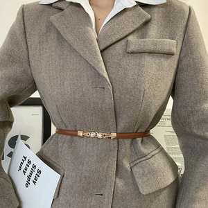 Détail d'une ceinture fine en cuir marron avec boucle perle et or sur blazer gris