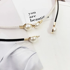 Detail of slim black and white patent leather belts with elegant pearl buckle decor