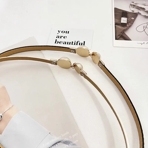 Detail showing elegant gold metal belt with white pearl buckle on black patent leather