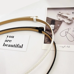 Close-up of minimalist black and white patent leather skinny belts with matching buckles