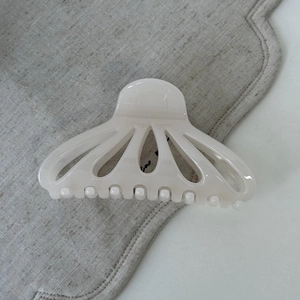 Close-up of cream fan-shaped hair claw with hollow design on textured grey linen