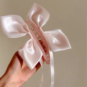 Dettaglio della pinza per capelli in raso rosa con lunghi nastri tenuta in mano