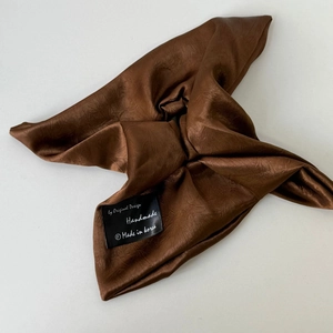 Detail of coffee brown satin hair tie with pleated texture and handmade label