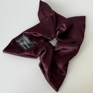 Close-up of deep wine red satin scrunchie with soft silk texture and handmade black woven label