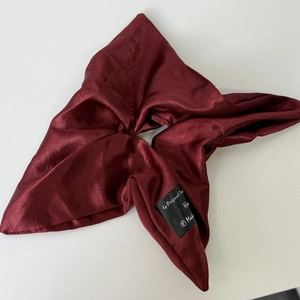 Detailed close-up of dark red satin scrunchie featuring a handmade woven label tag