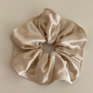 Detail view of champagne satin hair scrunchie with a handmade woven label and silky texture