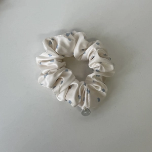 Detail eines Satin-Haargummis mit blauen Herzmustern und silbernem Metall-Logo