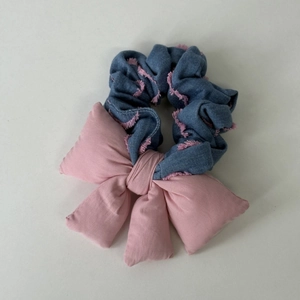 Détail d'un chouchou en denim bleu avec franges roses et un grand nœud en tissu