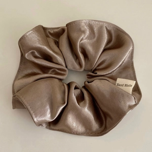 Detail of a brown satin scrunchie with a Hand Made tag on a minimalist grey background