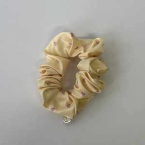 Detail eines gelben Satin-Scrunchies mit rosa Herzen und silbernem Metall-Anhänger