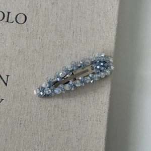 Detailed macro view of the silver BB hair clip with blue-gray crystals on linen texture