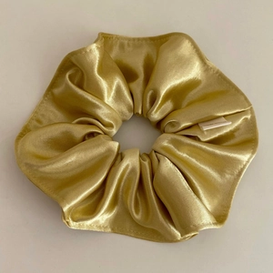 Detailed close-up of champagne gold satin scrunchie showing glossy texture and pleats
