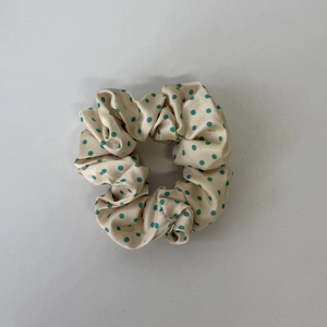 Detail eines großen beigen Scrunchies mit grünen Punkten und seidiger Satintextur