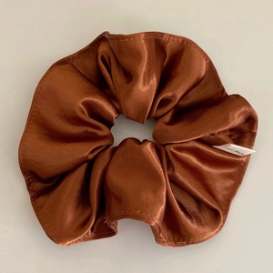 Close-up of caramel brown satin hair scrunchie with handmade label and pleated texture