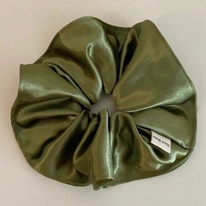 Detailed macro view of olive green satin scrunchie with smooth texture and hand made label
