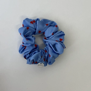 Nahaufnahme blaues Satin-Haargummi mit Herzmuster und silbernem Markenanhänger