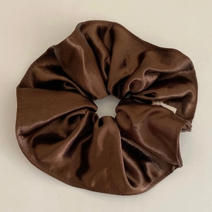 Detailed view of dark brown satin scrunchie with smooth texture and pleated design