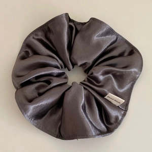 Detailed shot of dark grey satin scrunchie with a silk texture and 'Hand Made' woven label