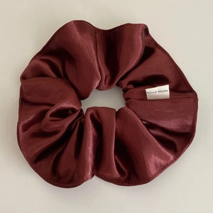 Close-up of deep red satin scrunchie with a handmade woven label and silky texture