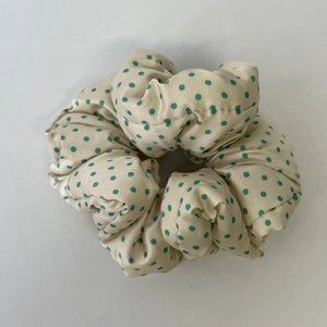 Detailansicht eines großen champagnerfarbenen Scrunchie mit grünen Punkten und Seideneffekt